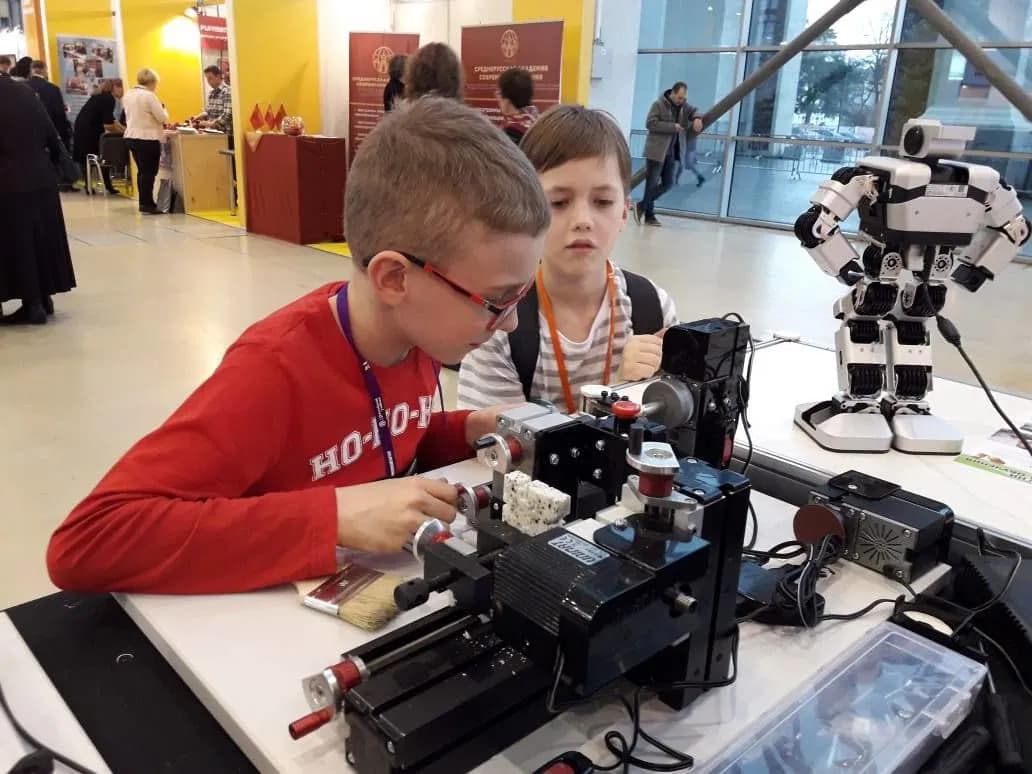 Two young boys intently operate a small tabletop machine at a science and technology exhibition.